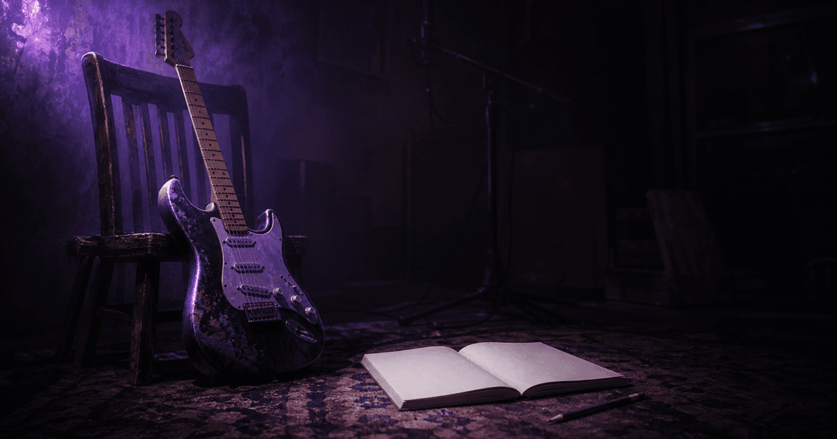 Electric guitar leaning on a chair beside an open blank notebook in a dark studio