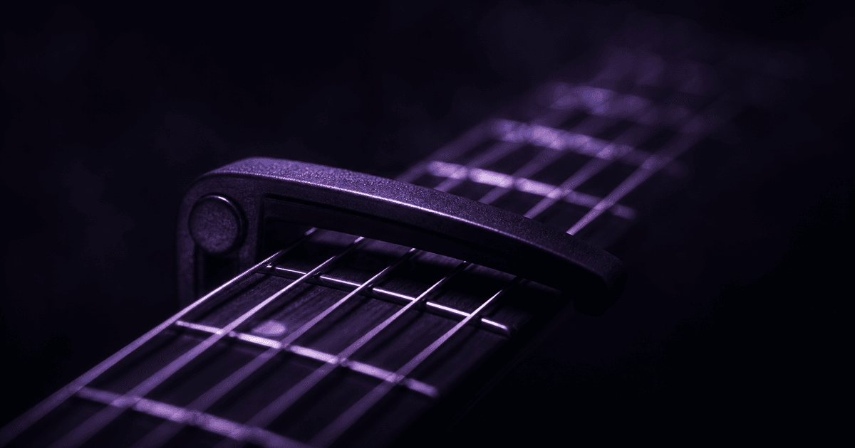 Capo clamped across a guitar fretboard, strings lit in deep purple shadow