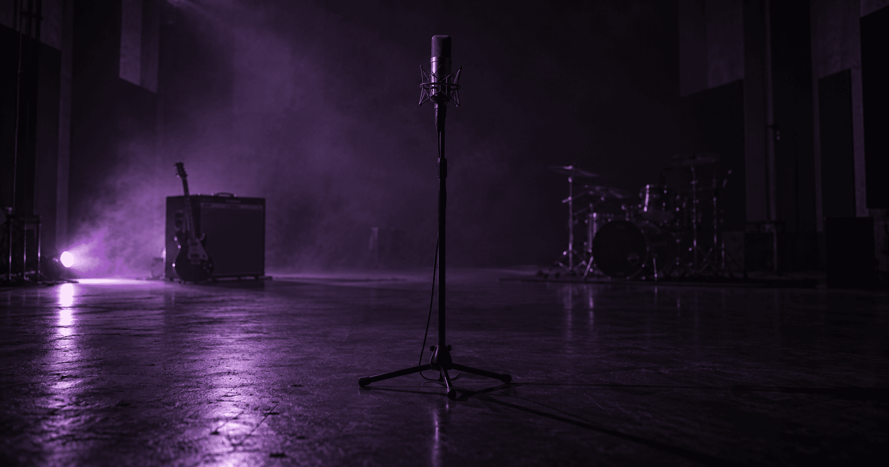 Lone condenser microphone facing a distant amp and drum kit in a dark purple studio room